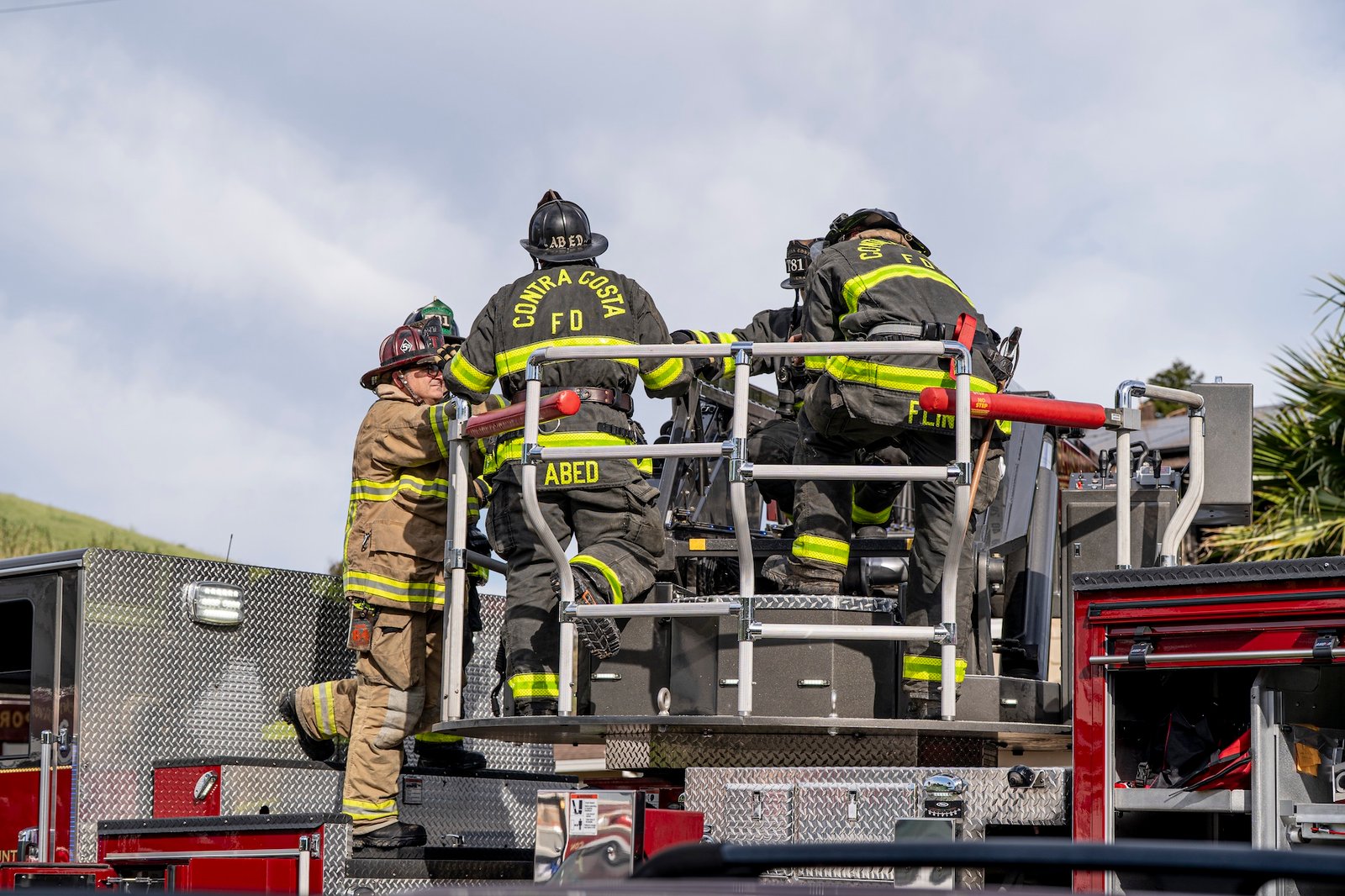 Firefighters standing on the back of a fire truck