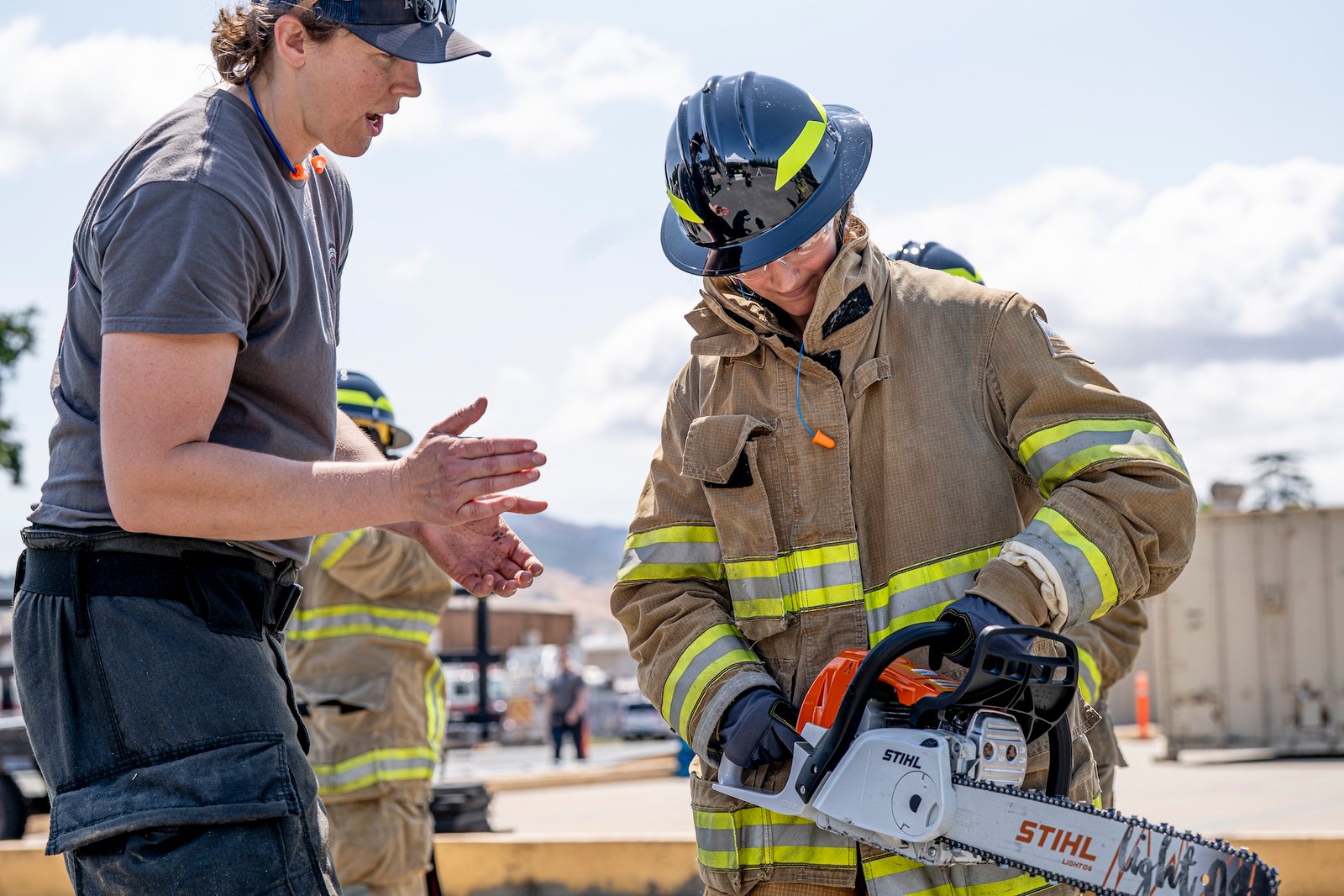 firefighter talking a camper through proper use of a chainsaw